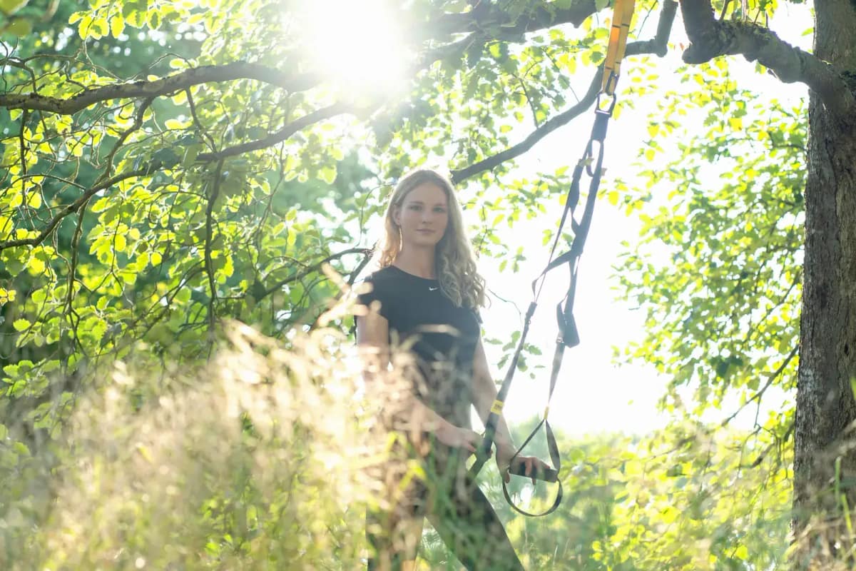 Lara Kölzow steht im sonnigen Park zwischen den Gurten eines Schlingentrainers